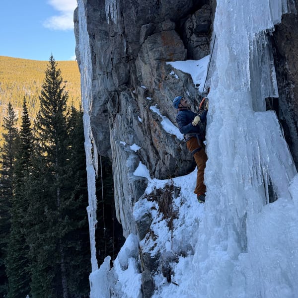 Ice climbing a frozen pillar, with pines on the slope below